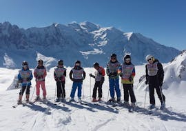 Esquiadores permanecen en línea frente a una montaña cubierta por la nieve como telón de fondo durante sus Clases de esquí para niños (8-12 años) - Vacaciones con la escuela de esquí ESF Chamonix.