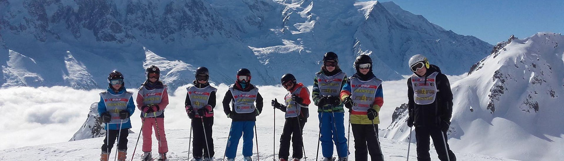 Skiers are standing in line in front of a snow-covered mountain landscape backdrop during their Kids Ski Lessons (5-12 years) - Low Season - Advanced with the ski school ESF Chamonix.