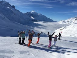 Skiers are standing in line in front of a snow-covered mountain landscape backdrop with their arms in the air during their Ski Lessons for Adults - All Levels with the ski school ESF Chamonix.