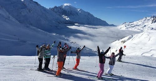 Cours de ski Adultes (dès 18 ans) à Chamonix - Centre avec ESF Chamonix Des skieurs se tiennent devant un paysage de montagnes enneigées avec leurs bras levés en l'air pendant leur Cours de ski pour Adultes - Tous niveaux avec l'école de ski ESF Chamonix.