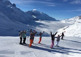 Skiers are standing in line in front of a snow-covered mountain landscape backdrop with their arms in the air during their Ski Lessons for Adults - All Levels with the ski school ESF Chamonix.