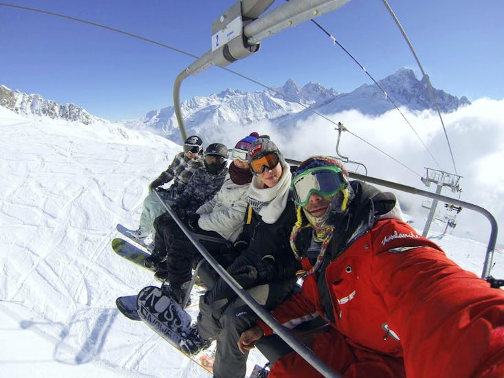 Een groep snowboarders zit in een stoeltjeslift die ze naar de top van de berg brengt waar ze hun Snowboardlessen voor Volwassenen - Alle Niveaus met ESF Chamonix beginnen.