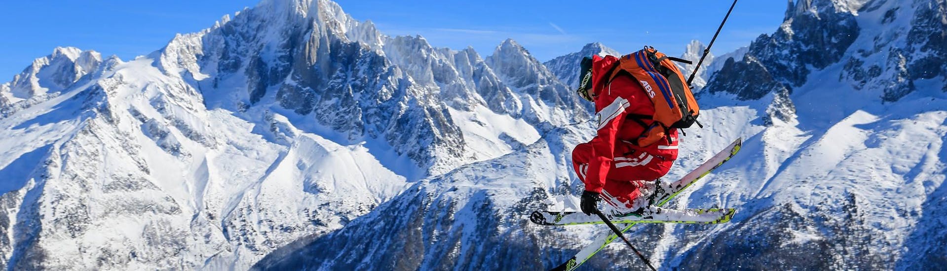 Sur fond de montagnes un skieur effectue un saut pendant qu'il faut du hors-piste pendant sa Sortie de ski freeride "Mont Blanc Ski Discovery" avec l'école de ski ESF Chamonix.