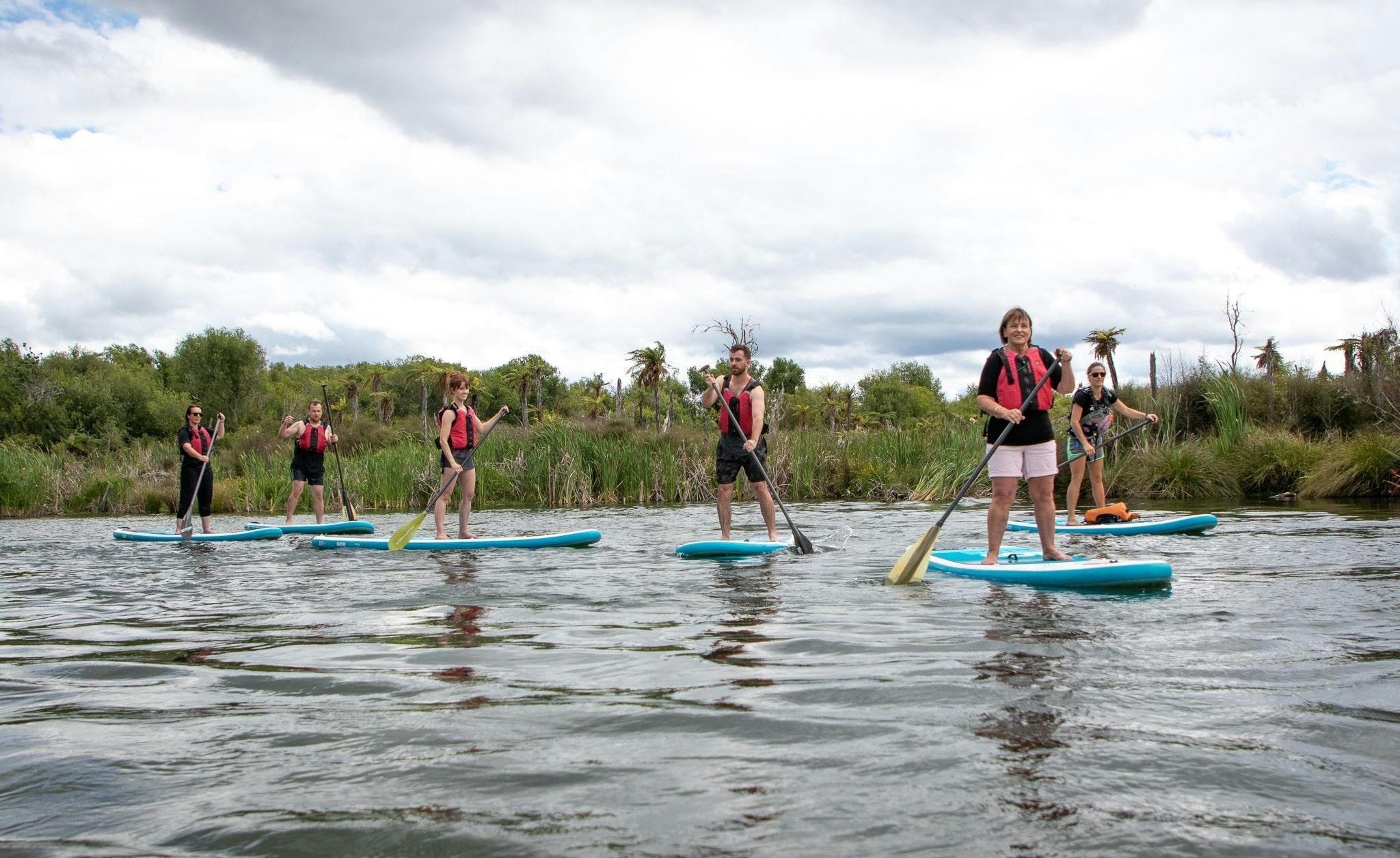 A family is enjoying the peaceful surroundings during Stand Up Paddle Boarding in Rotorua - Ohau Channel with Rotorua Rafting.
