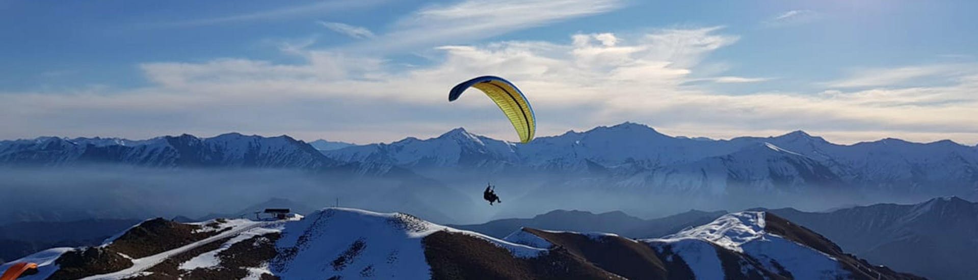 A paraglider from Skytrek Queenstown is flying over snow-capped mountains while Paragliding in Queenstown - Winter.