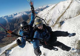 A tandem master from Skytrek Queenstown and his passenger are flying over the snow-capped peaks of Otago while Paragliding in Queenstown - Winter.