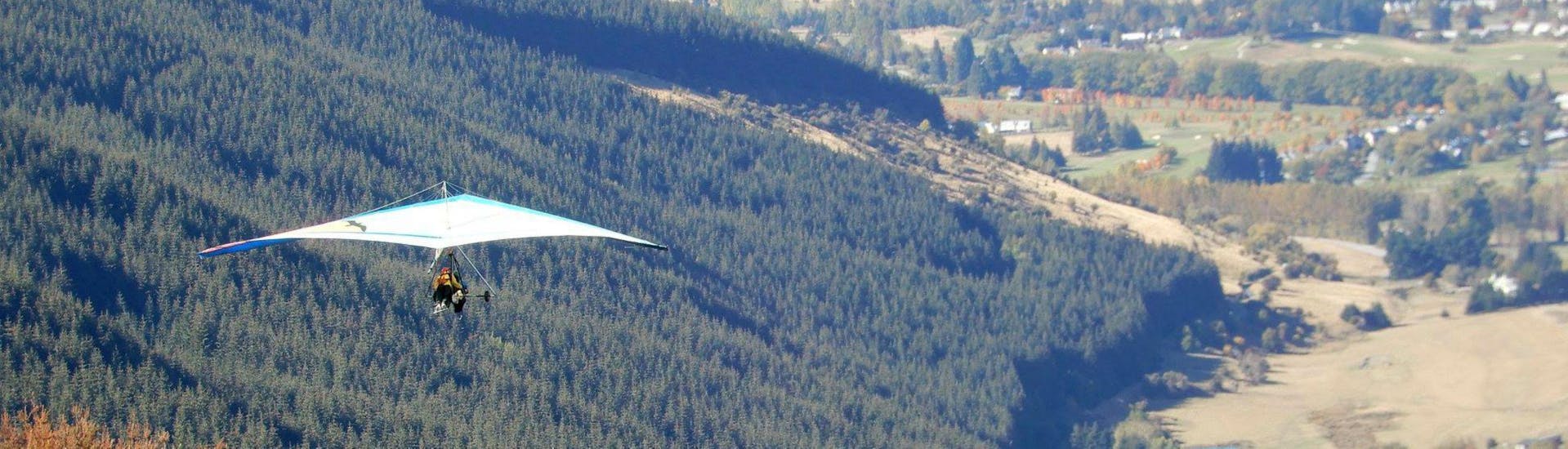 A hang glider from Skytrek Queenstown is gently floating above the woodland while Summer Hang Gliding in Queenstown.