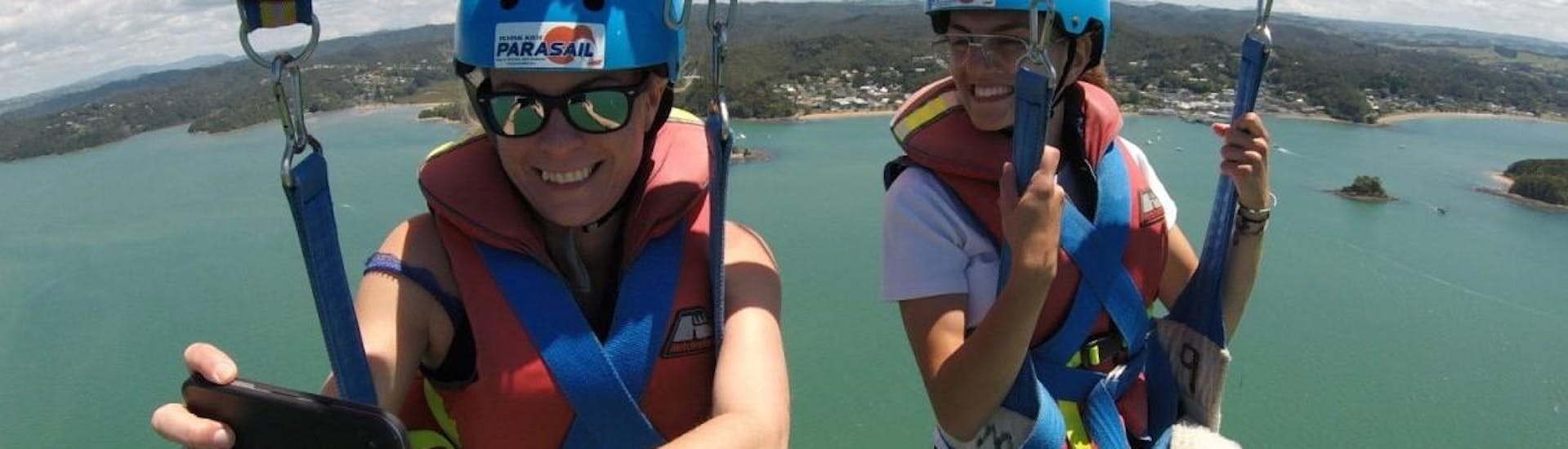 During the Parasailing in Paihia - For 2 People, two friends are enjoying the amazing views while being towed by a motorboat from Bay of Islands Parasail.