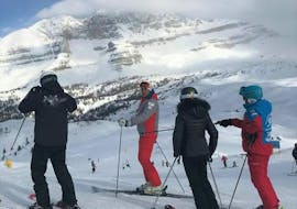 Een groep skiërs luistert aandachtig naar zijn skileraar tijdens de skilessen voor volwassenen - met ervaring georganiseerd door de skischool Scuola di Sci Val Rendena in het skigebied van Pinzolo.