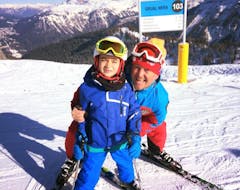 Ein Kind lächelt während dem von der Skischule Scuola di Sci Val Rendena organisierten Kinder Skikurs (3-5 J.) - Anfänger auf den Pisten von Pinzolo gemeinsam mit seinem Skilehrer in die Kamera.