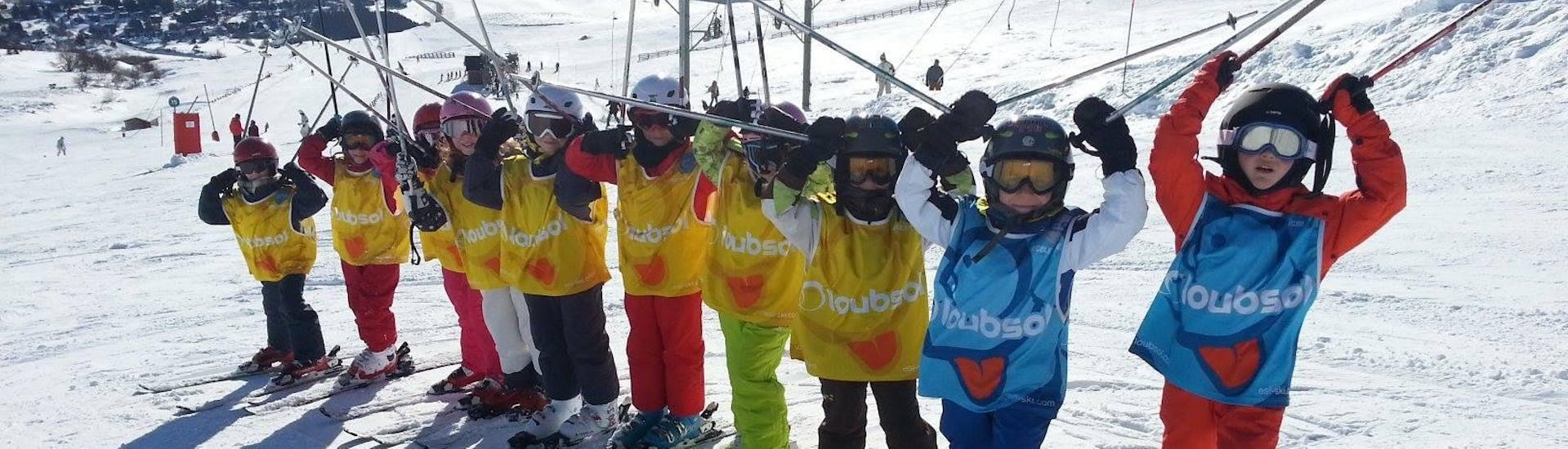 Kids are standing next to each other with their ski poles up in the air during their Kids Ski Lessons (5-12 years) - March 1-6 - All Levels with the ski school ESI Gliss'Émotion Super-Besse.