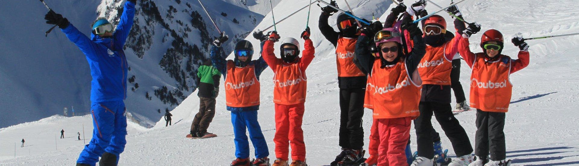 Unos jovenes esquiadores están parados uno al lado del otro con sus bastones de esquí en el aire durante sus clases de esquí para niños (5-13 años) - Tarde con la escuela de esquí ESI du Tourmalet en La Mongie. 