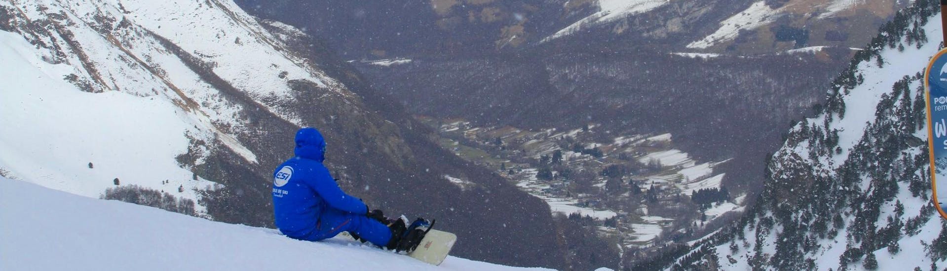Un snowboarder está sentado en la nieve contemplando el valle de abajo durante sus clases de snowboard para niños (a partir de los 8 años) con la escuela de esquí ESI du Tourmalet en La Mongie. 