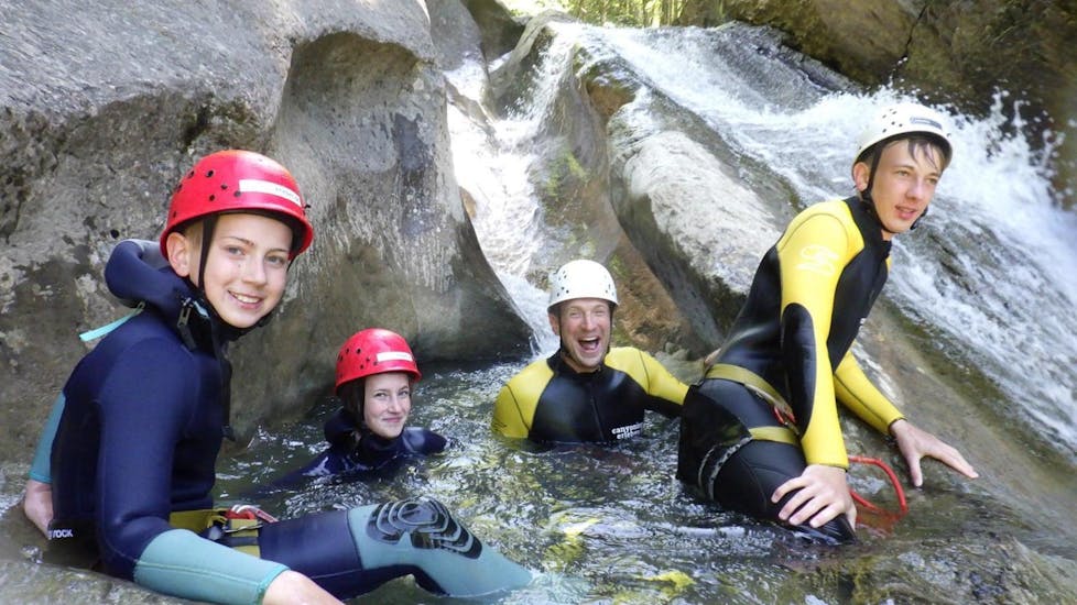 Ein Vater und seine drei Kinder lächeln beim Canyoning im Allgäu mit canyoning erleben in die Kamera während sie in einem Felsbecken sitzen.