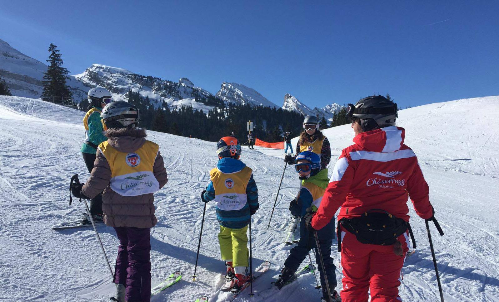 During the Kids Ski Lessons (5-15 years) - All Levels with Swiss Ski School Chäserrugg, a ski instructor and her group of young skiers are admiring the beautiful mountains of the Chäserrugg ski resort.