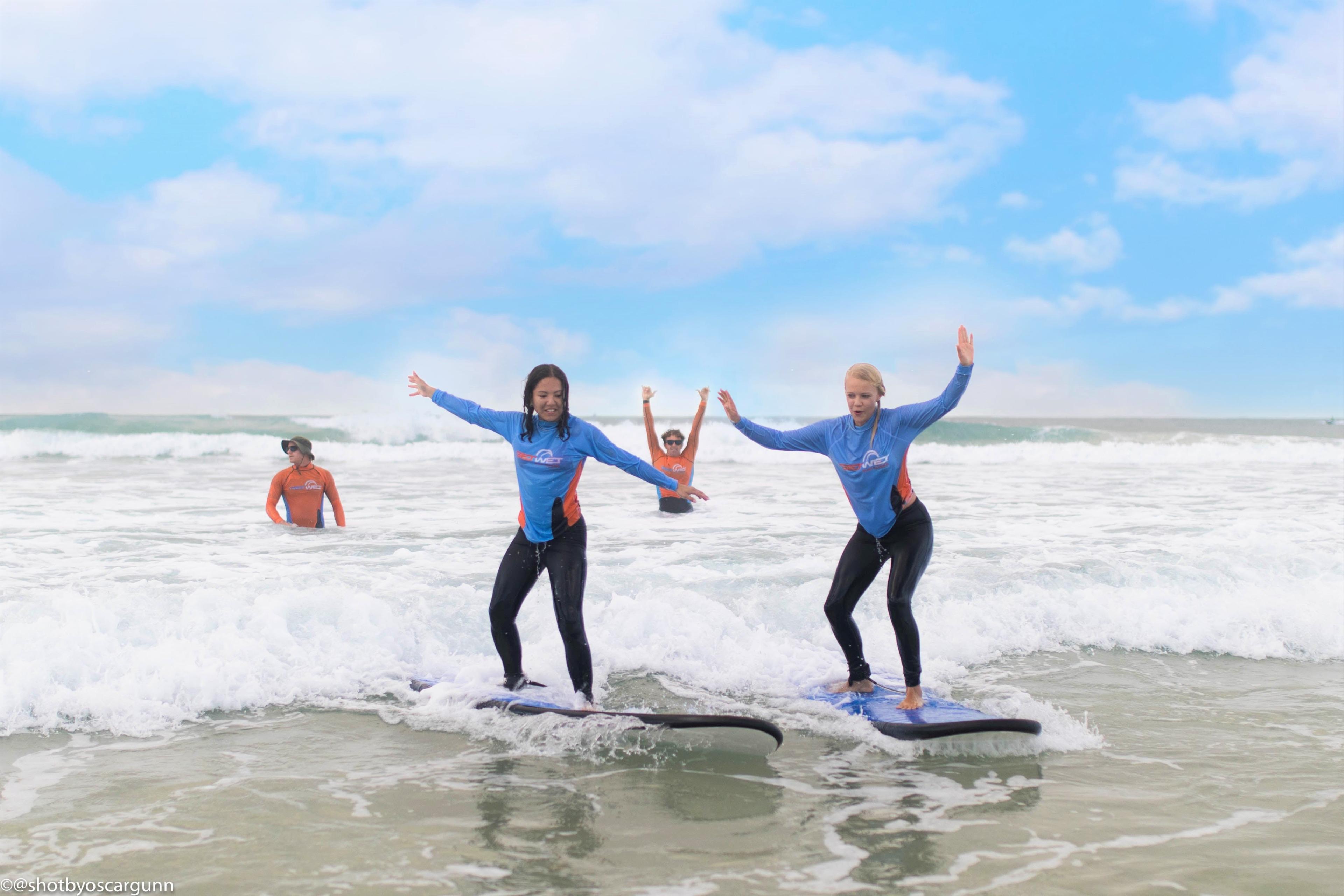 Two participants of the Surf Lessons in Gold Coast for Adults organized by the surf school Get Wet Surf School are having fun while riding a wave on the surfboard.