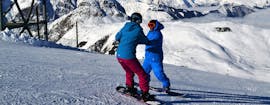 Un istruttore aiuta un giovane snowboarder a rimanere in equilibrio sulla sua tavola durante le lezioni private di snowboard per tutti i livelli a Les Deux Alpes con la Scuola Europea di Sci.
