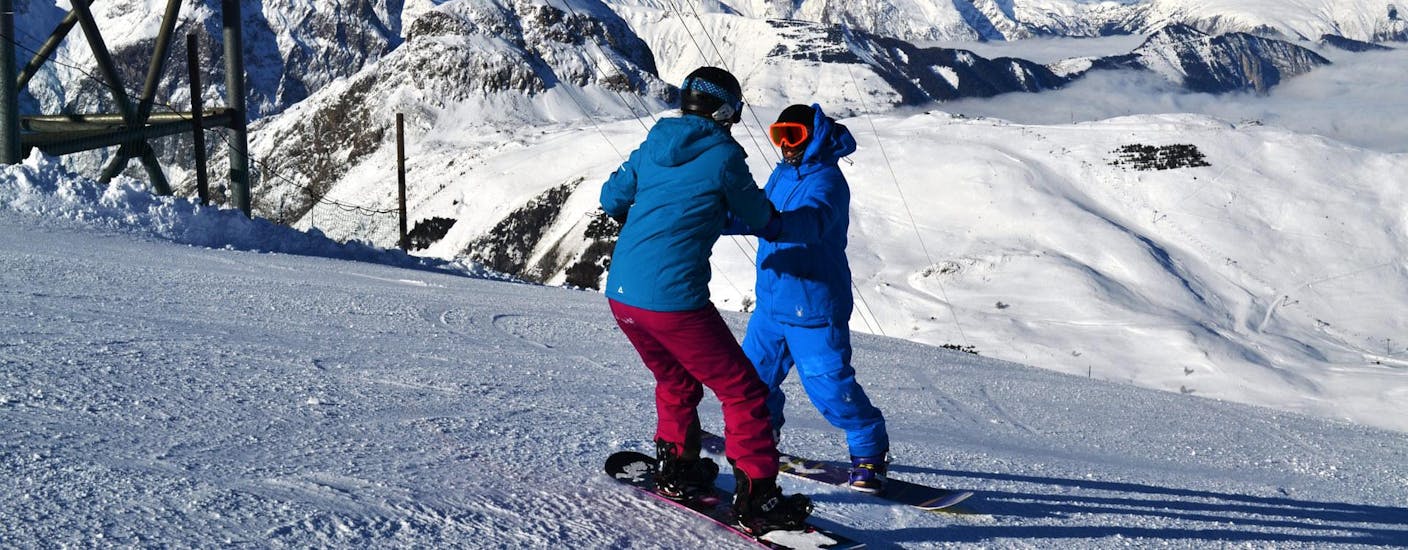 Un istruttore aiuta un giovane snowboarder a rimanere in equilibrio sulla sua tavola durante le lezioni private di snowboard per tutti i livelli a Les Deux Alpes con la Scuola Europea di Sci.