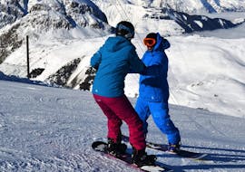 Un instructor ayuda a un joven snowboarder a mantener el equilibrio en su tabla durante las clases particulares de snowboard para todos los niveles, en Les Deux Alpes, con European Ski School.