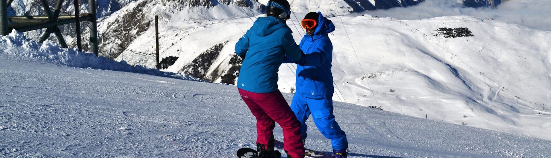 An instructor helps a young snowboarder stay balanced on his board during private snowboarding lessons for all levels in Les Deux Alpes with the European Ski School. 