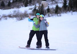 Während des Angebotes "Privater Snowboardkurs für Kinder & Erwachsene - Abends" organisiert von Maestri di Sci Cristallo - Monte Bondone im Skigebiet Monte Bondone lächelt eine Snowboarderin gemeinsam mit ihrem Privatlehrer in die Kamera.