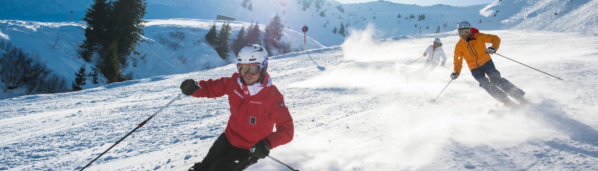 Dans le cadre des Cours de ski pour Adultes - Avec Expérience, un moniteur de ski de l'école de ski Skischule Kitzbühel Rote Teufel montre à son groupe la bonne technique de ski.
