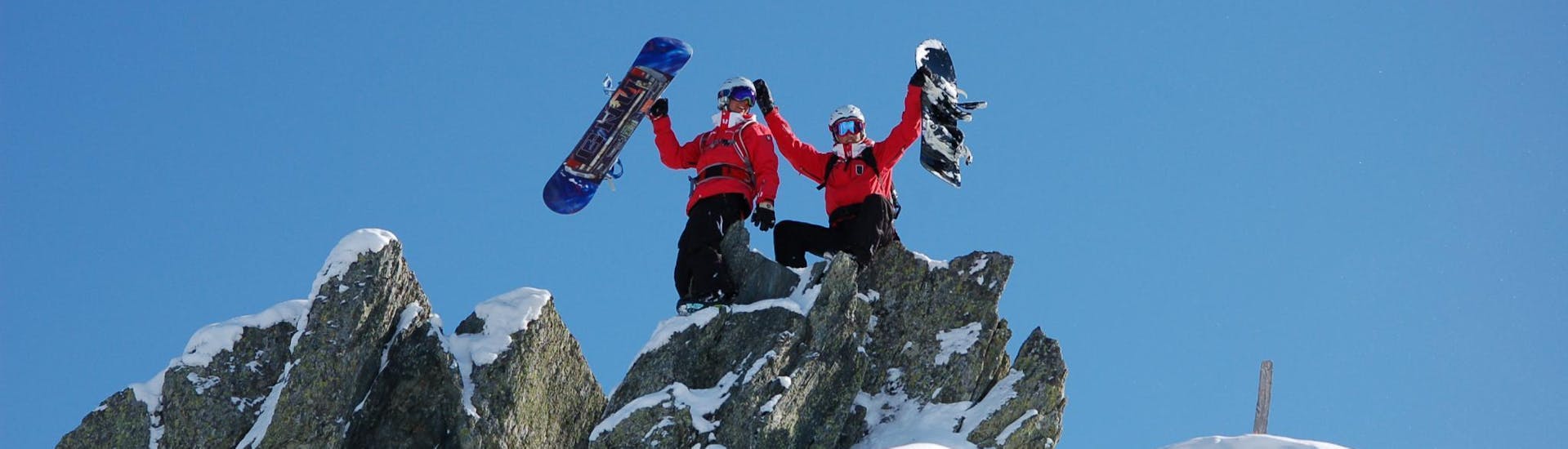 In the Snowboarding Lessons for Kids & Adults - With Experience two snowboard instructors of the ski school Skischule Kitzbühel Rote Teufel climbed on a rock and are posing for a photo with their snowboards.