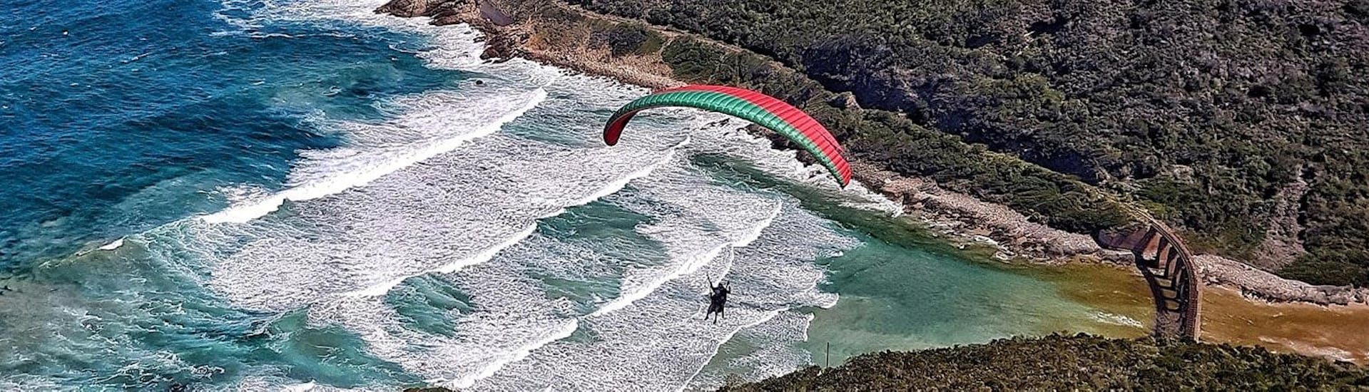 A tandem pilot from Dolphin Paragliding is landing with a client during the Paragliding in Wilderness - Adventure Flight at a beach.