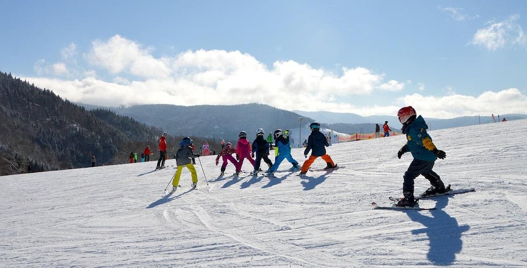 Several kids are skiing down a slope during their Kids Ski Lessons (5-12 years) - Weekend - All Levels with the ski school Moonshot La Bresse.