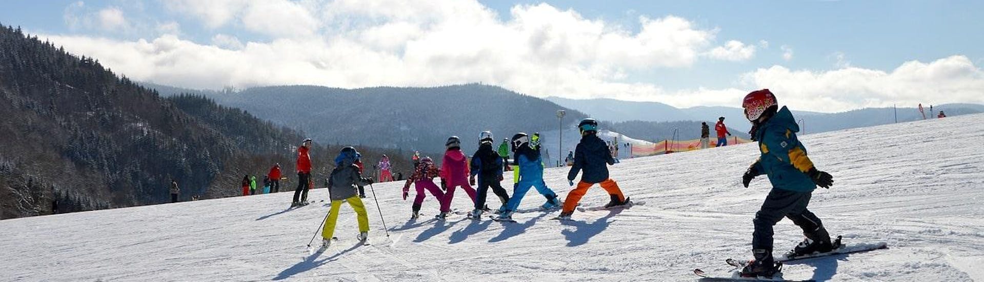 Beim Kinder Skikurs (5-12 Jahre) - Wochenende - Alle Levels der Skischule Moonshot La Bresse fahren mehrere Kinder die Skipiste hinunter.