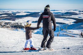 Un moniteur de ski de l'école de ski Evolution 2 Super Besse tient la main d'un enfant en haut des pistes avant de commencer leur Cours particulier de ski pour Enfants - Tous âges.