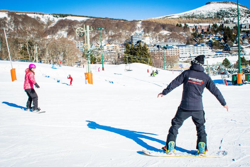 Un snowboardeur apprend les bases du snowboard avec l'aide de son moniteur de snowboard de l'école de ski Evolution 2 Super Besse pendant son Cours particulier de snowboard pour Enfants & Adultes.