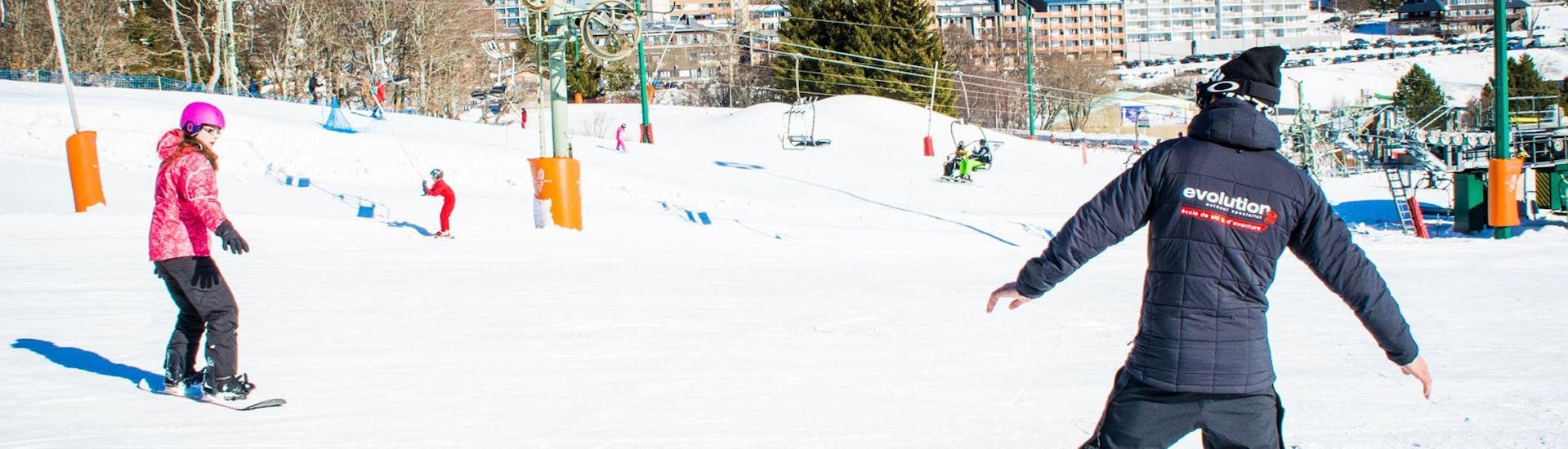 Un snowboardeur apprend les bases du snowboard avec l'aide de son moniteur de snowboard de l'école de ski Evolution 2 Super Besse pendant son Cours de snowboard pour Enfants (dès 8 ans) - 1er cours.