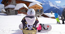 Un enfant est assis dans la neige avec la planche de snowboard attachée à ses pieds en attendant le début de son Cours de snowboard pour Enfants (dès 8 ans) - 1er cours avec l'école de ski Evolution 2 Super Besse.