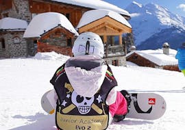 A child is sitting in the snow with the snowboard attached to their feet before starting their Snowboarding Lessons for Kids (from 8 years) - 1st Timer with the ski school Evolution 2 Super Besse.