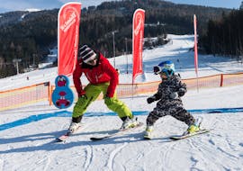 An instructor of Skischule Innsbruck is showing a little kid how to ski in snowplough during kids ski lessons "Superminis".