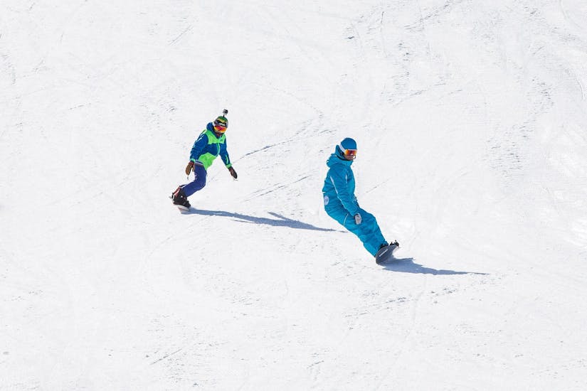 Un snowboardeur suit son moniteur de snowboard de l'école de ski ESI Snow Diam's le long d'une piste enneigée pendant son Cours particulier de snowboard - Crest-Voland.