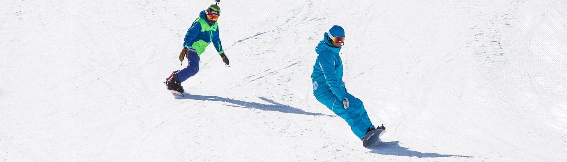 Un snowboardeur suit son moniteur de snowboard de l'école de ski ESI Snow Diam's le long d'une piste enneigée pendant son Cours particulier de snowboard - Crest-Voland.
