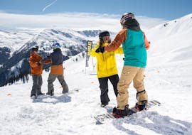 A snowboard instructor helps the course participant to find the balance during the snowboarding lessons "Basic" for kids and adults of the snowboard school BOARD.AT.