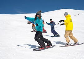 A group of snowboarders ride down the snowy slope in slalom during the snowboarding lessons "Basic - LTR Package" - beginner from the snowboard school BOARD.AT