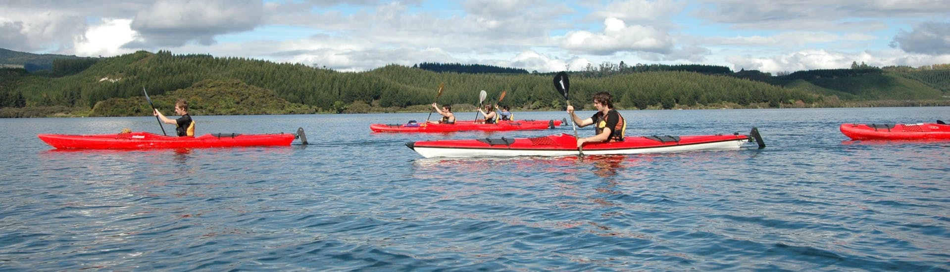 A group of people paddle in three kayaks on the calm lake during their kayak rotorua guided hot pools - winter - lake rotoiti with River Rats Rotorua Raft & Kayak.