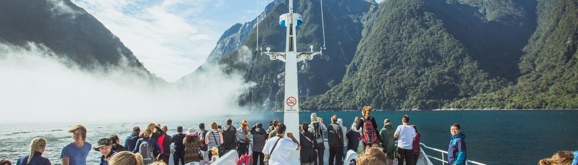 During the Coach Tour with Milford Sound Cruise at Sunrise travellers are gathered at the deck of an luxurious catamaran operated by Jucy Cruise.