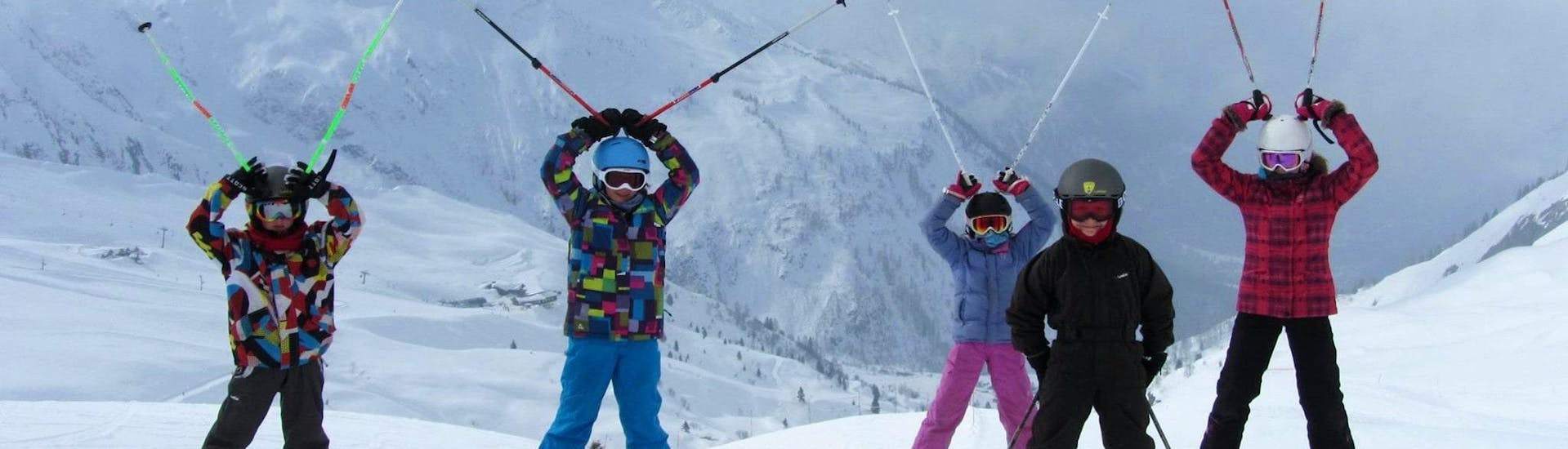 Kids are standing at the top of the mountain with their ski poles up in the air during their Kids Ski Lessons (5-12 years) in Chamonix/Savoy with the ski school ESF Chamonix.