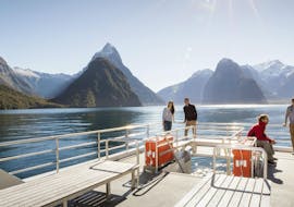 A group of people is standing on the outdoor viewing deck of one of the Southern Discoveries boat during their Encounter Nature Cruise in Milford Sound.