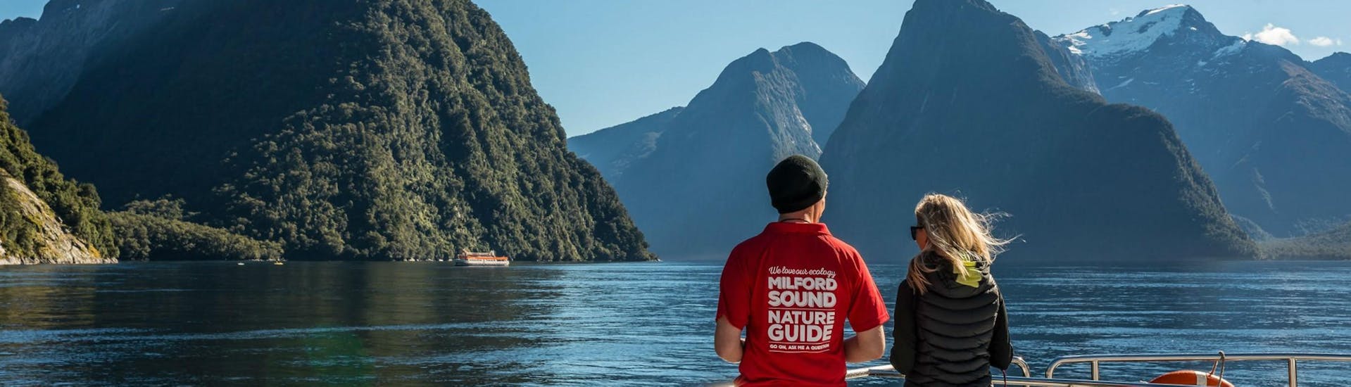 A nature guide and a passenger are taking in the spectacular scenery from the viewing deck of a Southern Discoveries catamaran during their Milford Sound Nature Day Trip from Queenstown.