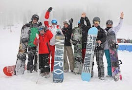 Un groupe de participants aux cours de snowboard pour enfants et adultes - tous niveaux, organisés par l'école de ski Scuola di Sci Sauze Sportinia, pose pour une photo sur les pistes de la station de ski de Via Lattea.