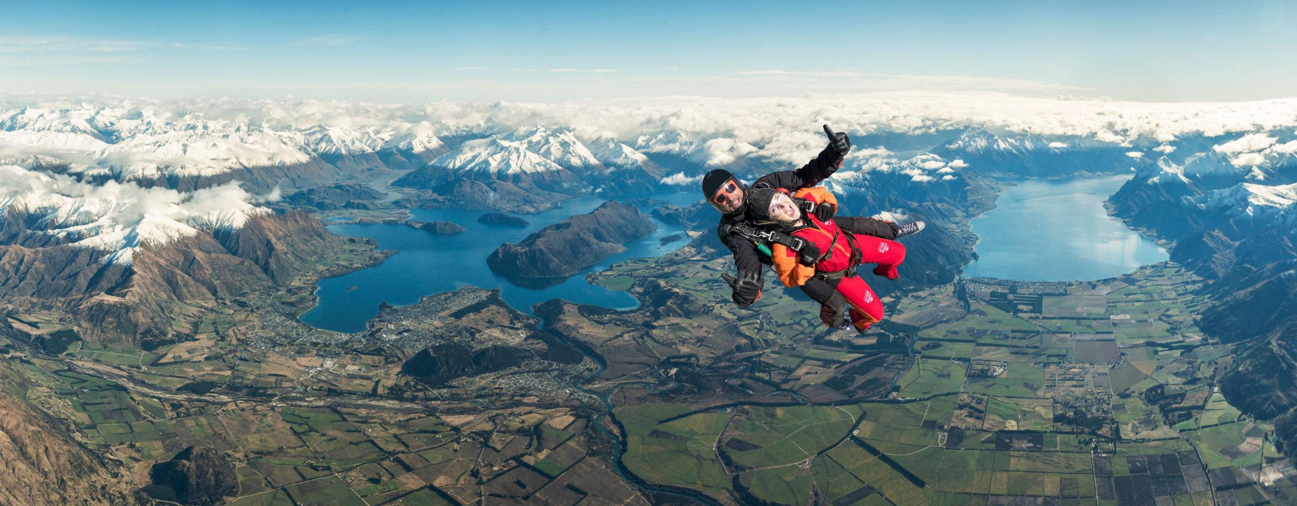 A tandem master from Skydive Wanaka and his passenger are in the middle of their Tandem Skydive in Wanaka - 12,000ft with Queenstown Transfer, above the spectacular mountainscape around Lake Wanaka.