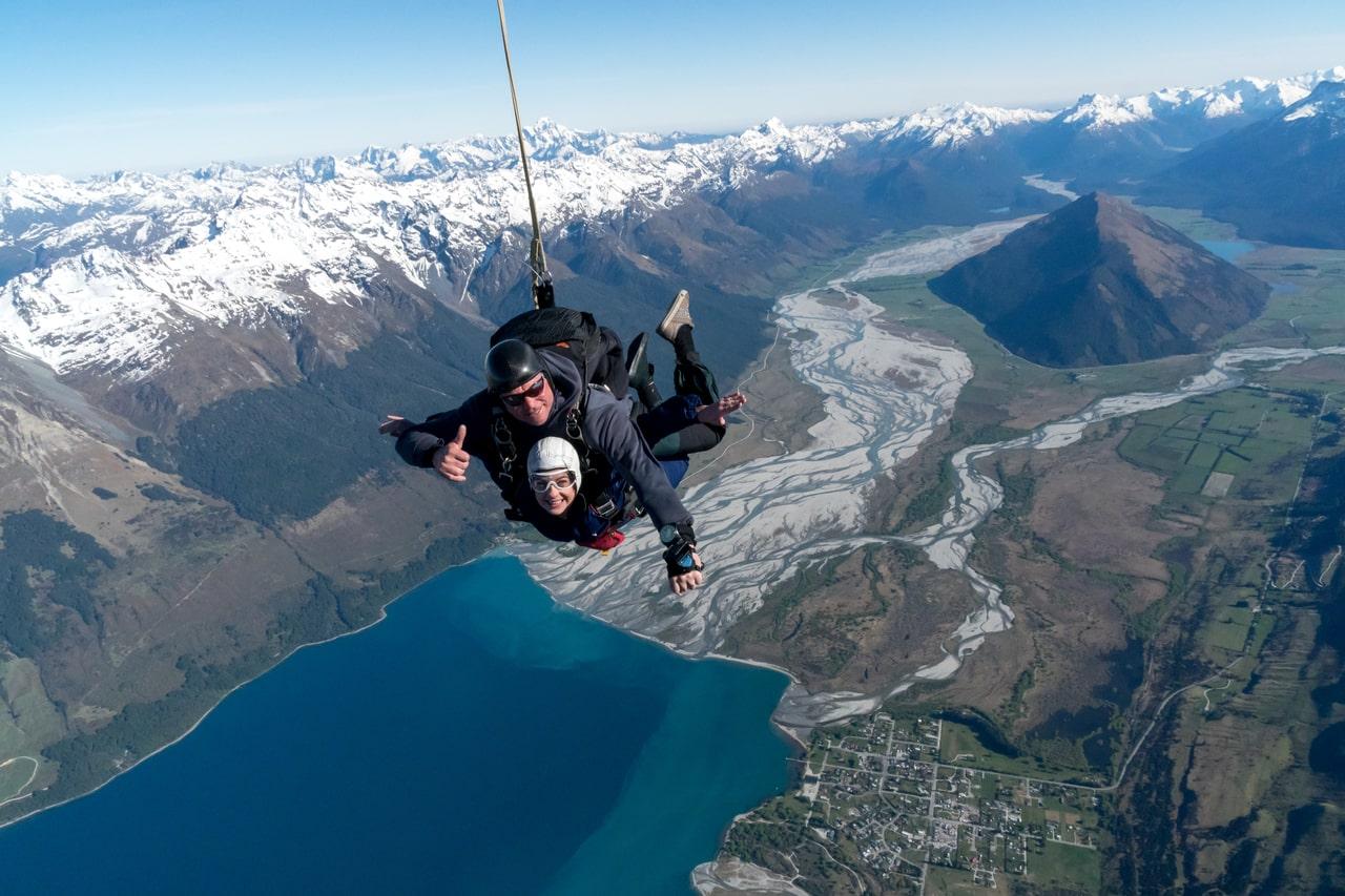 A tandem master from Skydive Southern Alps Queenstown and his passenger are smiling at the camera during their Tandem Skydive in Queenstown - 12,000ft over the Dart River estuary near Glenorchy.