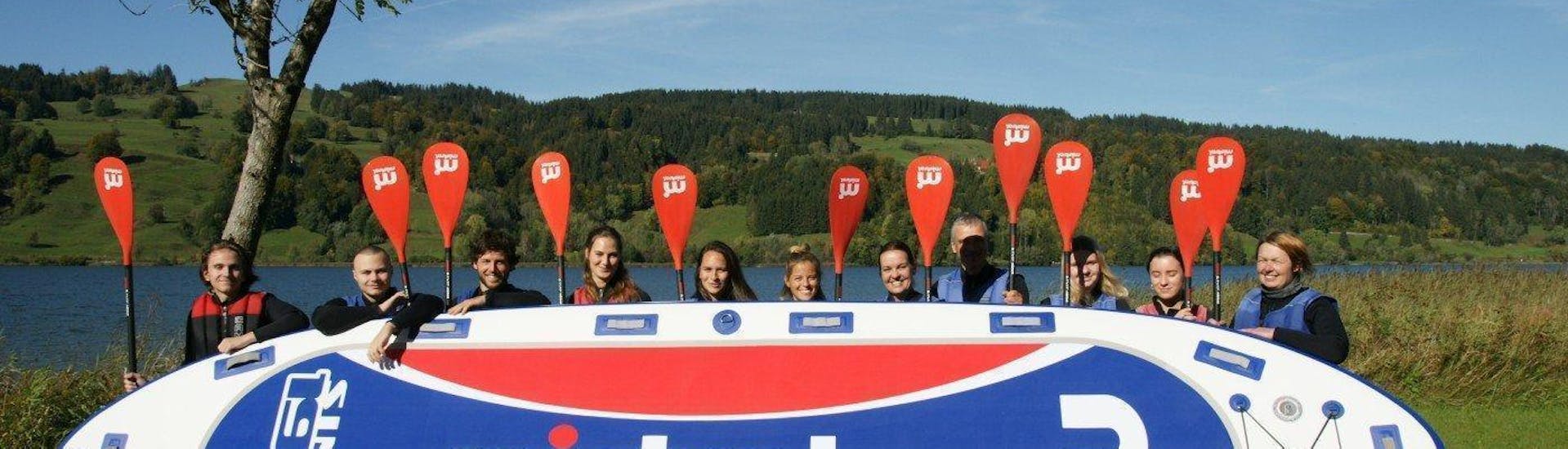 A group of friends standing behind the big SUP board that was used on the big stand up paddeling tour in Allgäu with Spirits of Nature Allgäu.