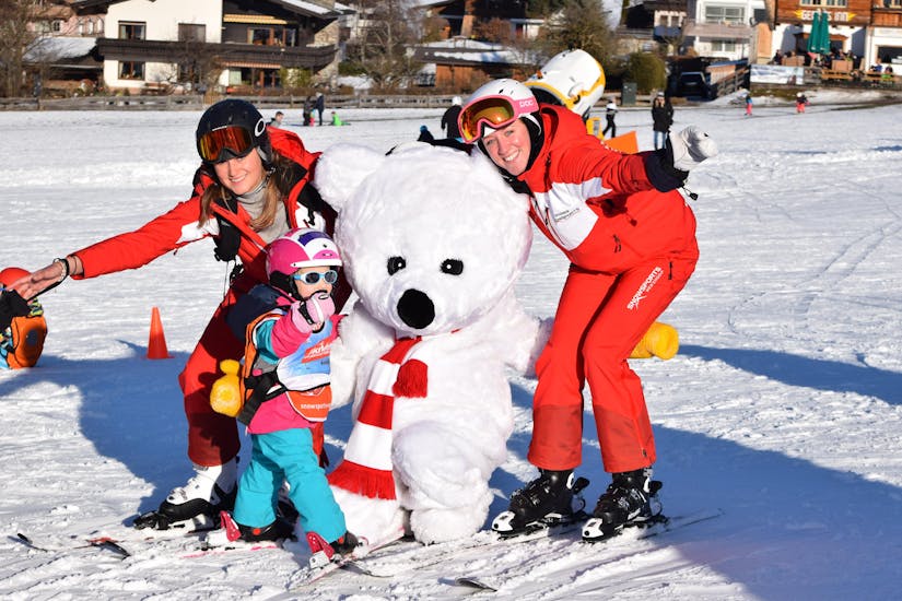 Twee skileraren, een kind en Billy de ijsbeer tijdens de Kids Skilessen "Bambini" (3-4 jaar) voor alle niveaus met skischool Snowsports Westendorf.